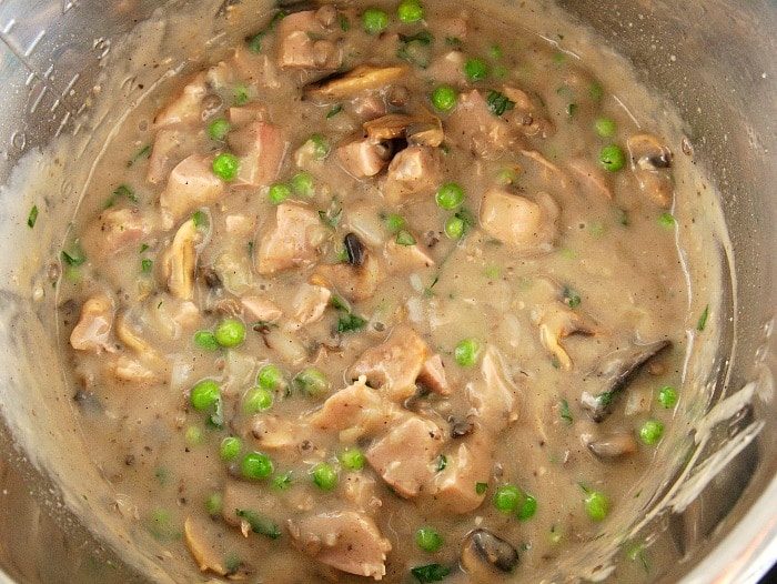 A pot of creamy homemade cream of mushroom, brimming with tender pieces of chicken, peas, and mushrooms.