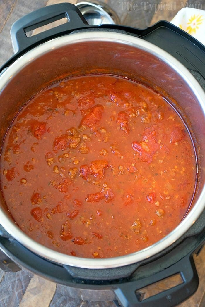 An open Instant Pot reveals a hearty sauce simmering with tomatoes and ground meat, reminiscent of a robust spaghetti sauce.