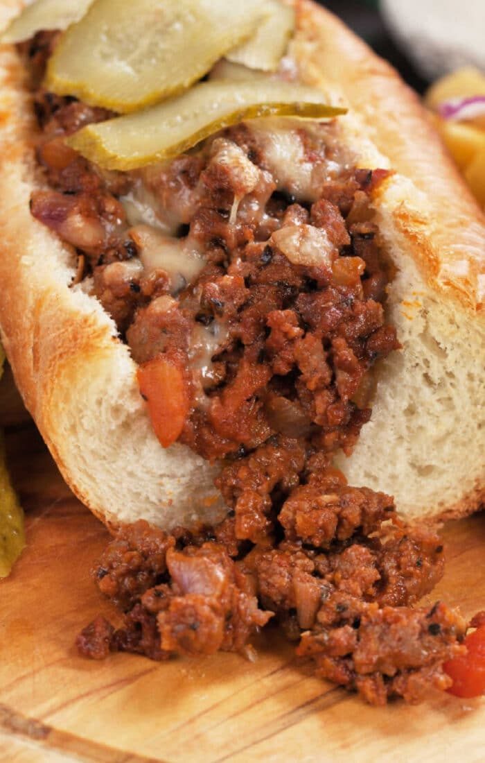 A hoagie with seasoned minced meat, reminiscent of homemade Sloppy Joes recipes, topped with pickle slices, sits enticingly on a wooden board.
