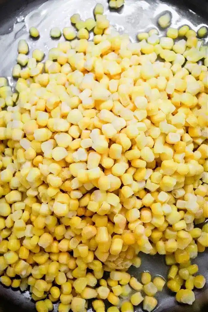 A close-up view of a heap of fresh or possibly frozen yellow and white corn kernels, piled on a dark surface, promises the good potential of Honey Butter Skillet Corn.