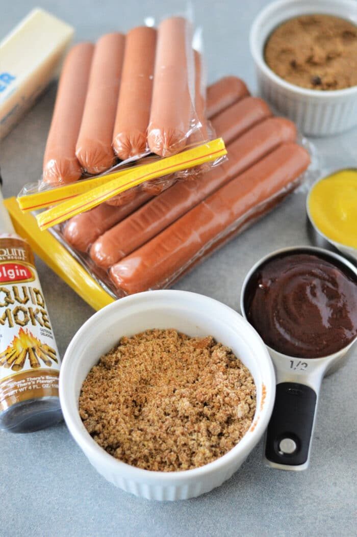 The countertop is a culinary stage set with essential ingredients: hot dogs, brown sugar, liquid smoke, mustard, and barbecue sauce, all ready to create mouthwatering hot dog burnt ends.