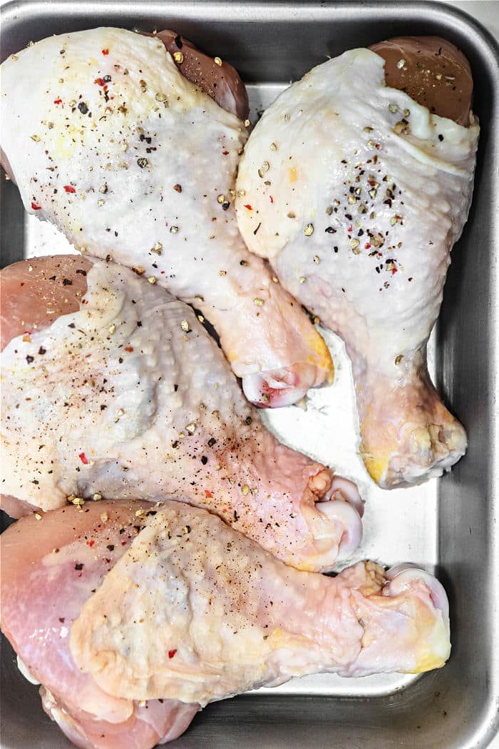 Chicken drumsticks, seasoned with salt and pepper, rest enticingly in a metal baking tray.
