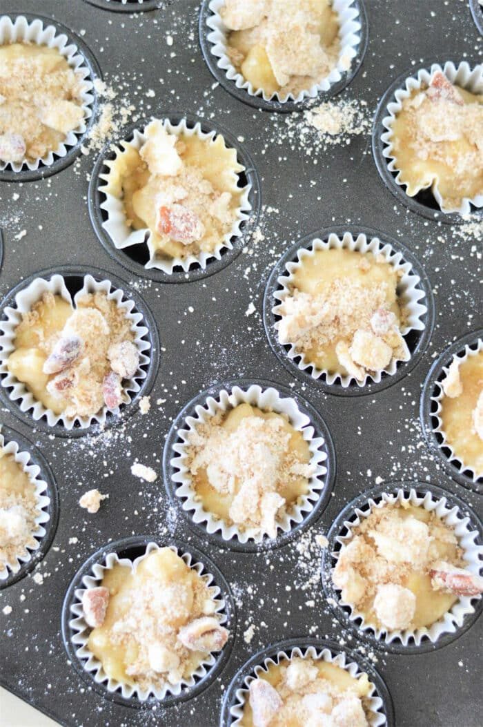 cupcake batter with crumb topping sits in a tray of lined muffin cups, ready to bake. Wondering how long to bake mini cupcakes? adjust the time slightly for solid results.
