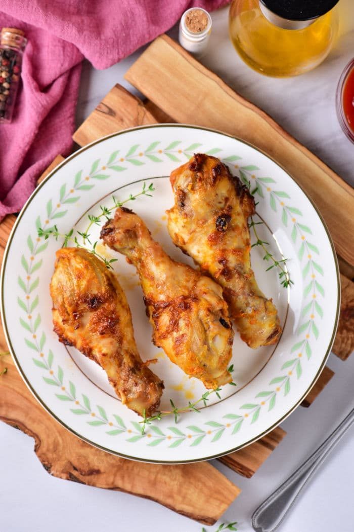 A plate of chicken drumsticks, perfectly timed after learning how long to boil chicken legs for tender flavor, is garnished with herbs. Set on a rustic wooden board against a pink cloth backdrop, it's a feast for both the eyes and the palate.