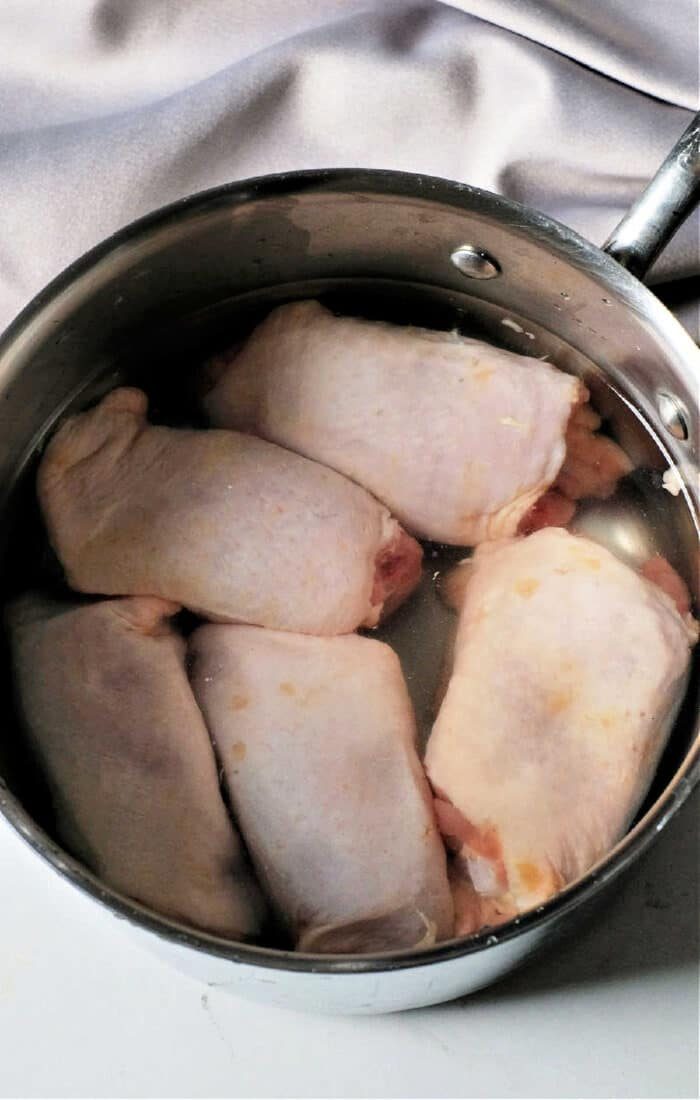 Raw chicken thighs sit in a stainless steel pot, preparing for the next step—wondering how long to boil chicken thighs for the solid tenderness.
