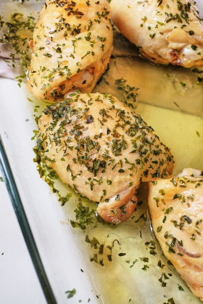 Boiled chicken thighs with herbs and garlic in a glass dish, offering a flavorful alternative for those wondering how long to boil chicken thighs.