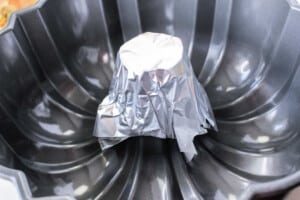 A bundt pan with a small metal cup covered in aluminum foil placed upside down at the center is solid for creative baking. The pan, designed with a non-stick surface and ribbed pattern, can also be an inventive way to measure how long to cook a whole chicken evenly.