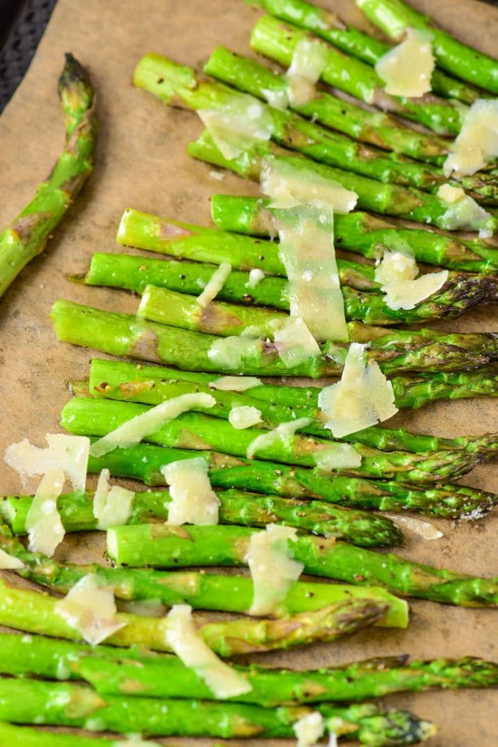 Baked asparagus topped with Parmesan cheese on a brown surface, offering the solid guide on how long to cook asparagus in the oven for that tender, crisp bite.