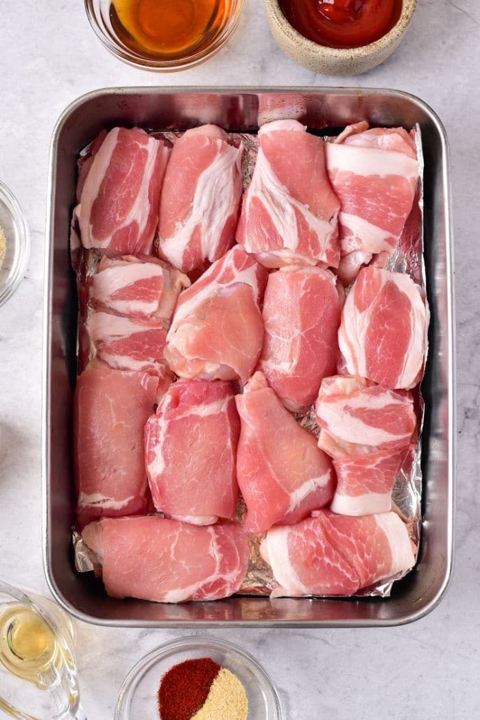 chicken wings wrapped with bacon arranged neatly in a metal tray, surrounded by small bowls of condiments and spices. While savoring this sight, you might also wonder how long to cook chicken wings in the oven at 375 for that solid balance of tenderness and flavor.