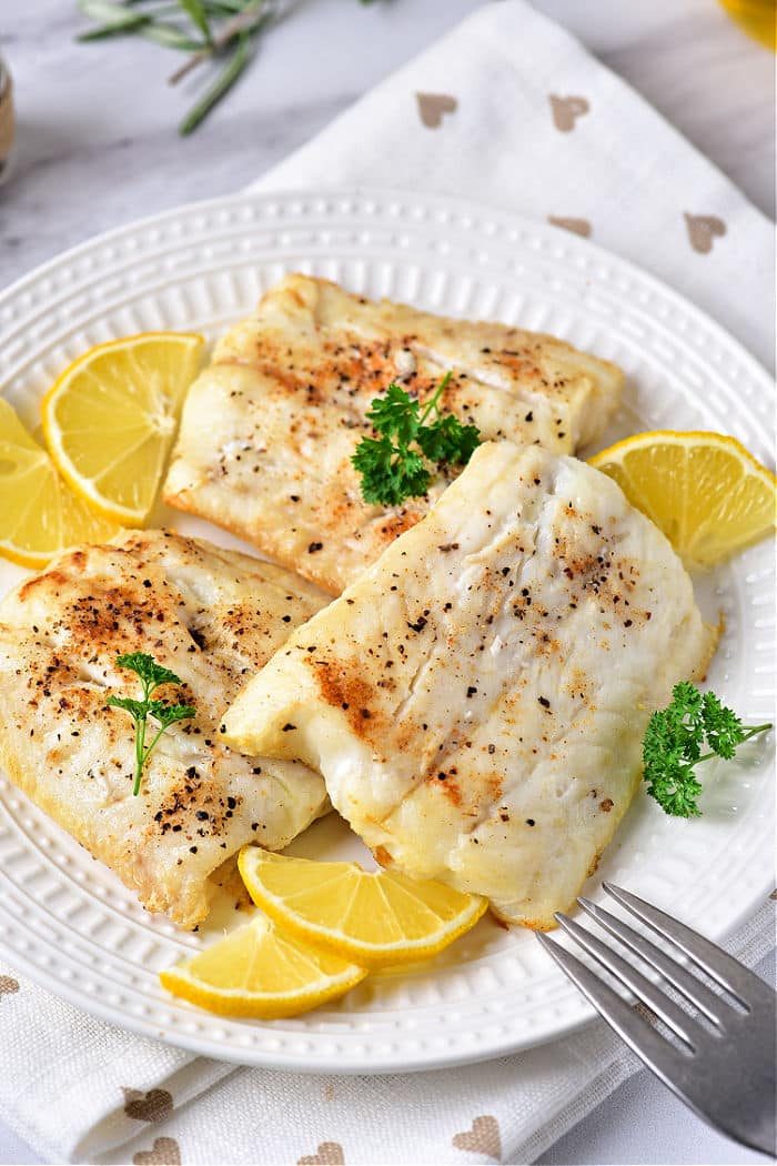 baked cod fillets delicately cooked to perfection, paired with lemon slices and parsley on a white plate.
