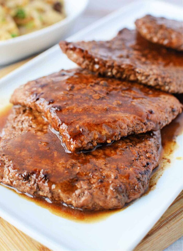 Juicy, cooked cube steak slices with sauce on a white plate invite curiosity about how long to cook cube steak in a frying pan for that solid tenderness.