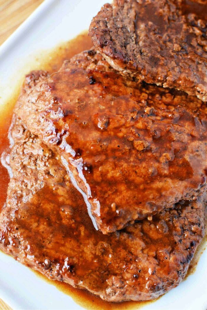 Close-up of juicy, cooked cubed steaks in rich brown gravy on a white plate, reminiscent of perfectly timed cube steaks in a frying pan.