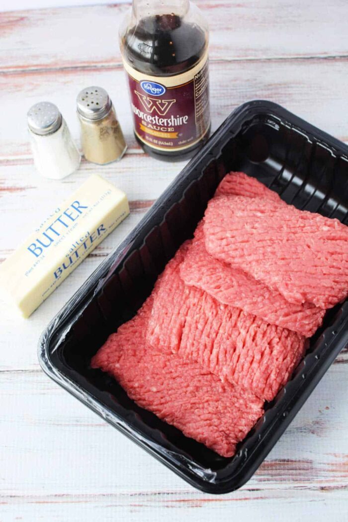 Ingredients for a recipe: cubed steak, Worcestershire sauce, butter, salt, and pepper on a white wooden surface. Wondering how long to cook cube steak in a frying pan?.