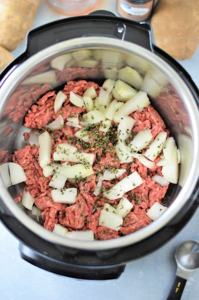 An overhead view of raw ground beef, chopped onions, and seasoning in an Instant Pot, ready to be cooked. Wondering how long to cook ground beef? This combination ensures a delightful meal in no time.