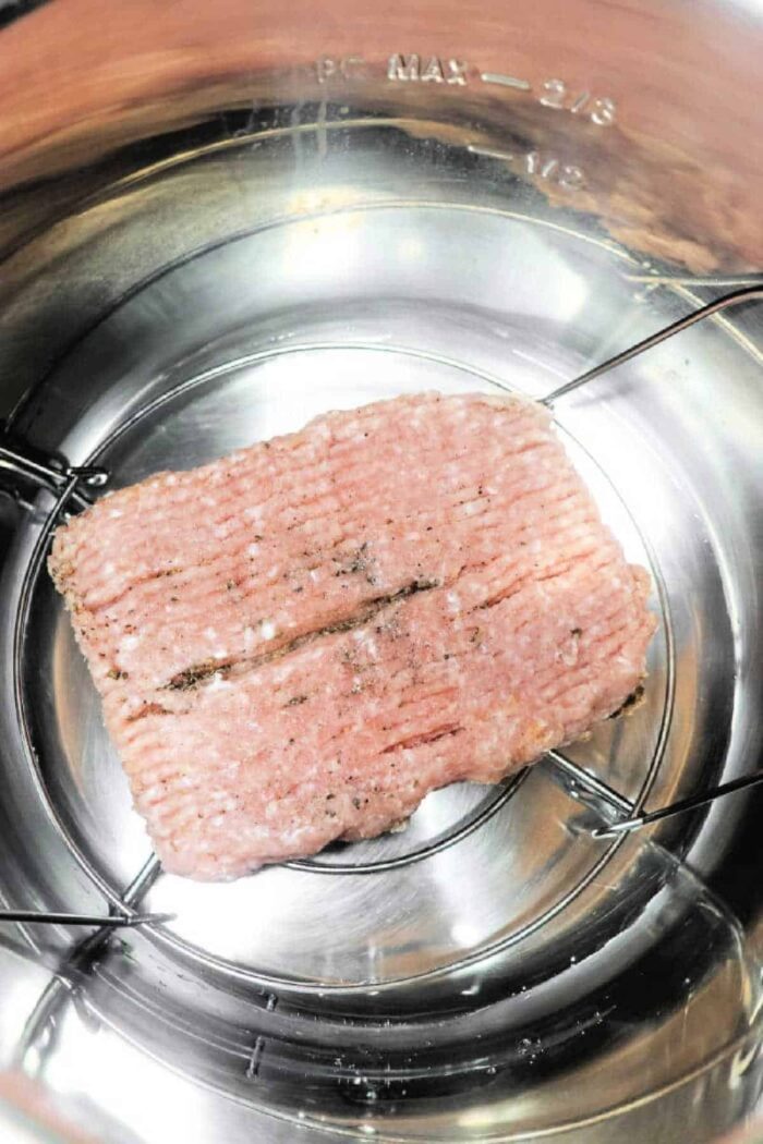 Ground chicken on a metal trivet inside an Instant Pot, ready for cooking. Wondering how long to cook ground chicken? You'll find it cooks quickly and evenly, making meal prep a breeze.