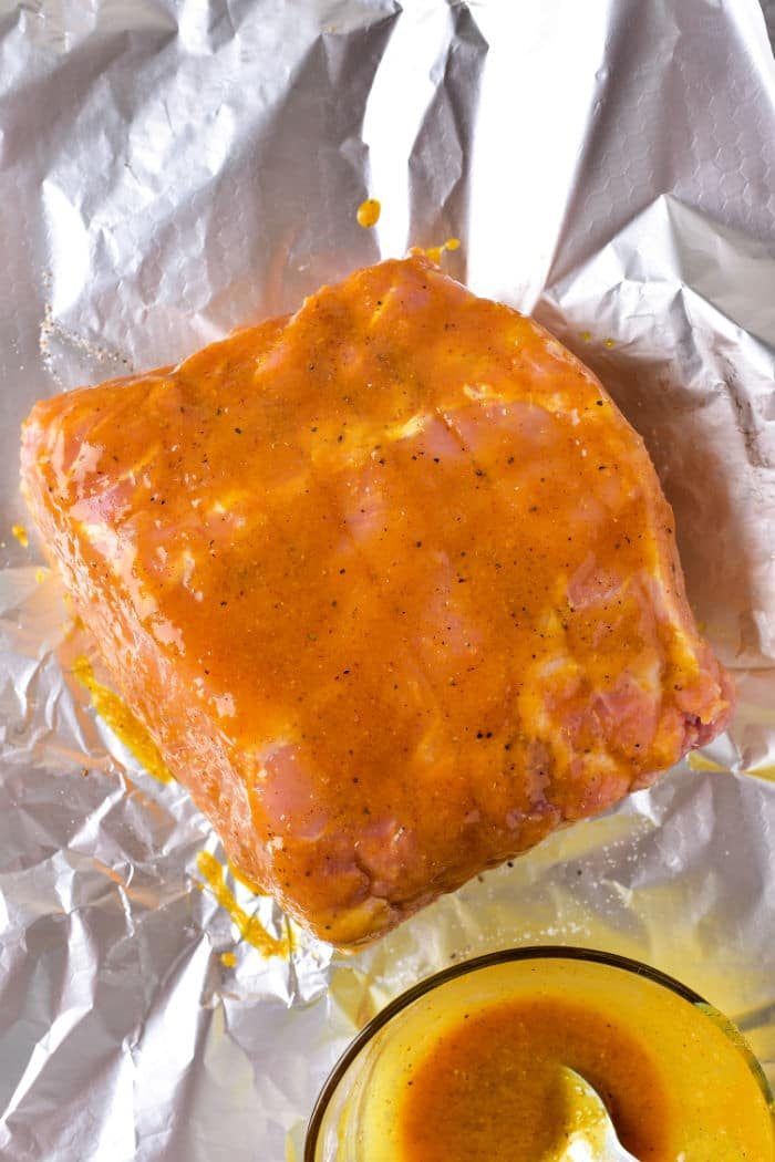 Raw pork roast coated in a bright mustard marinade sits on aluminum foil, with a bowl of the marinade beside it, ready to be transformed like learning how long to cook a pork roast in the oven at 375 degrees