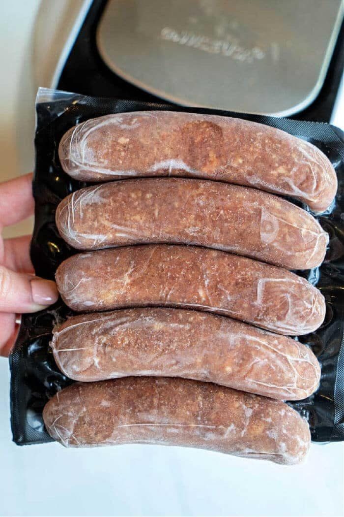 A hand holds a vacuum-sealed pack of five uncooked Italian sausages, solid for cooking as flavorful Italian sausage in oven recipes.