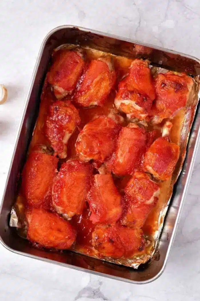Chicken wings covered in a red sauce, possibly marinara or barbecue sauce, sits on a light-colored countertop to bake in oven.