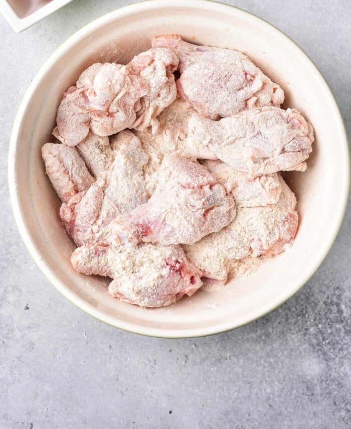 Raw chicken wings coated in baking powder sit in a white bowl on a gray surface, the solid start for learning how to bake crispy chicken wings.