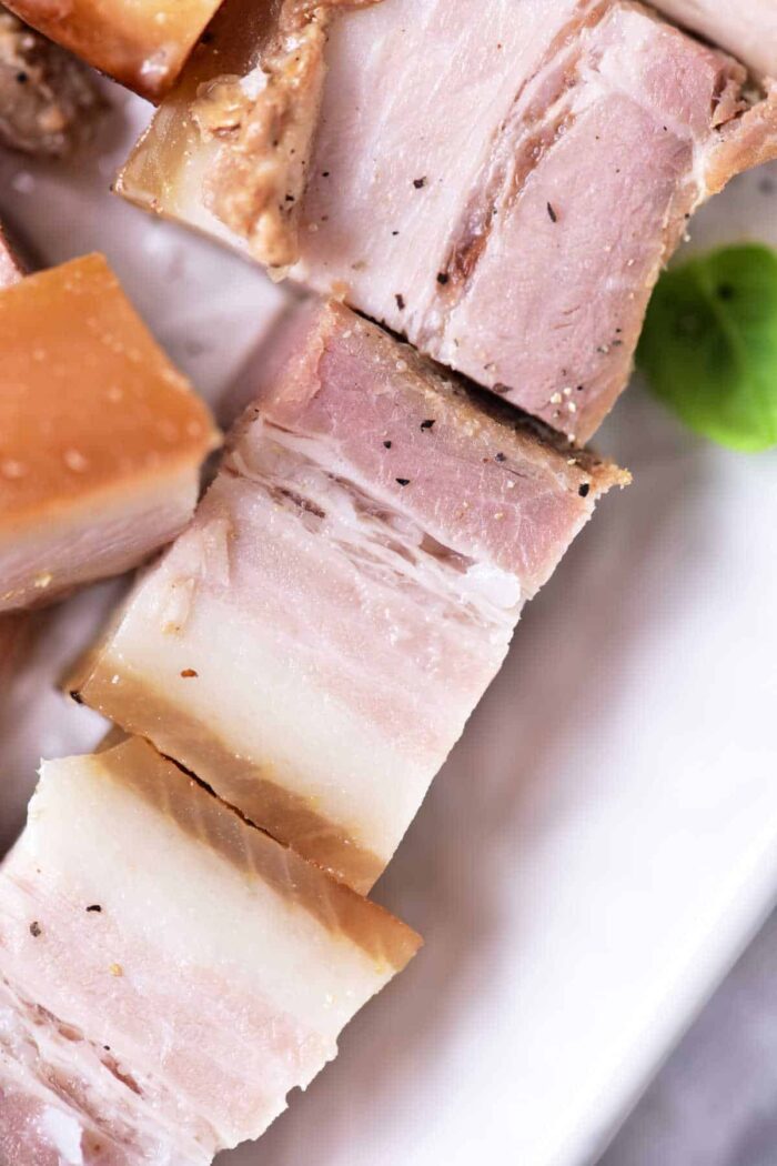 Close-up of sliced pork belly on a plate, showcasing layers of fat and meat, a good result reminiscent of the techniques used in how to confit pork.