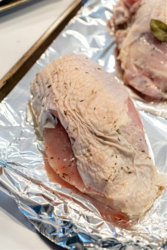 Raw turkey breast pieces seasoned with herbs rest on a foil-lined baking sheet, ready for roasting. Their marbled surface gleams with visible skin and spices. This method mirrors techniques seen in "How to Cook a Butterball Turkey Breast," ensuring tender, flavorful results each time.