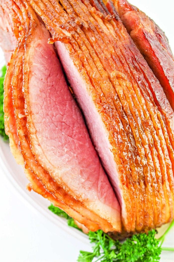Close-up of a sliced, glazed ham served on a platter with parsley garnish, showcasing the delightful results of how to cook a spiral ham in the oven.