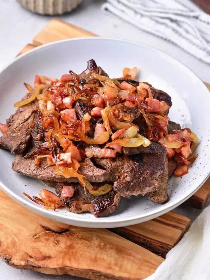 A white bowl filled with cooked liver pieces topped with sautéed onions and diced bacon bits.