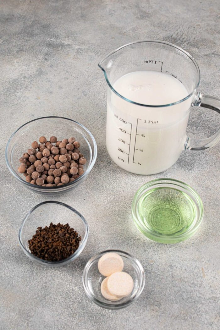 Ingredients on a table are milk in a measuring cup, chocolate chips, instant coffee, mint oil, and two tablets—a solid setup to learn how to cook boba for bubble tea.