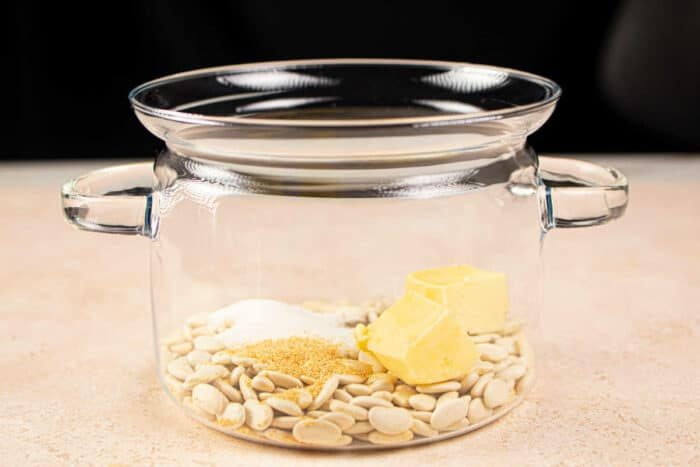 A glass pot with butter beans, butter, sugar, and spices inside rests on a light surface. Its reminiscent of preparing a comforting dish like butter beans—simple yet satisfying in its blend of ingredients.