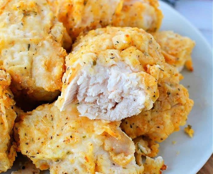 A plate of golden brown, air fryer-fried chicken breast pieces, one with a bite taken out, reveals the tender white meat inside.