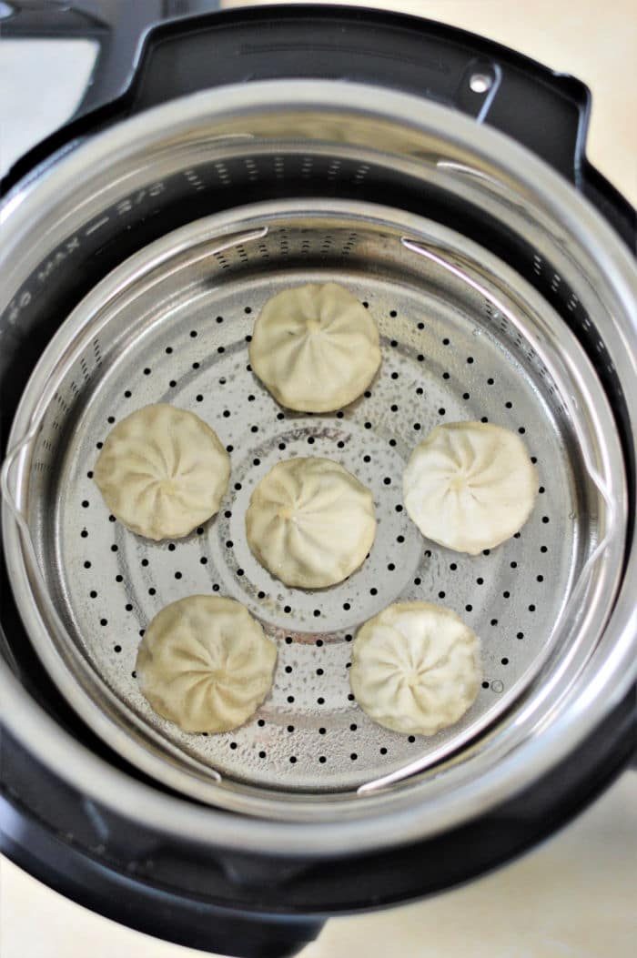 Six dumplings steam gently in a stainless steel basket inside instant pot, revealing the simple art of cooking frozen dumplings to perfection.