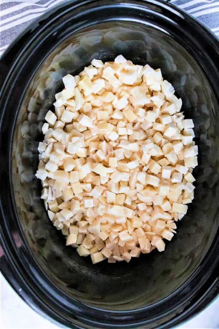 Diced frozen potatoes inside a slow cooker on a striped cloth backdrop, offering a hint of how to cook frozen hash browns with ease.