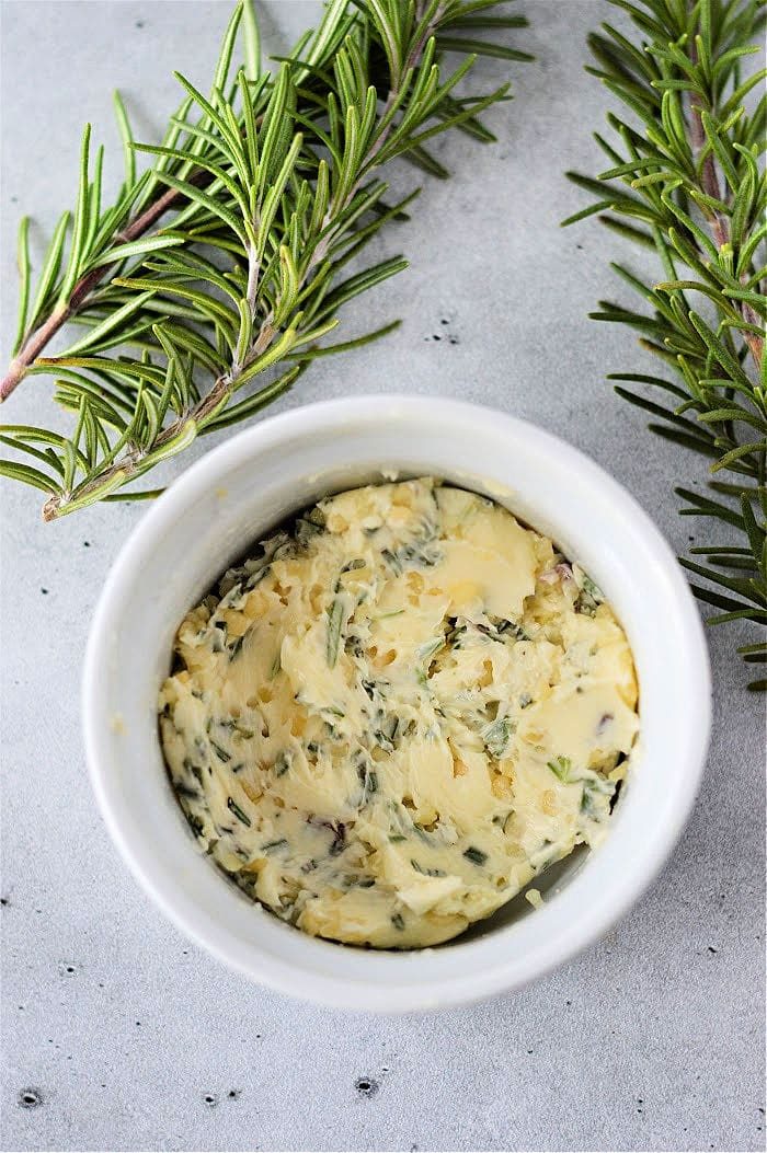 Herb-infused butter in a white ramekin, garnished with fresh rosemary sprigs on a light gray surface, is the solid complement when you learn how to cook frozen steak to perfection.