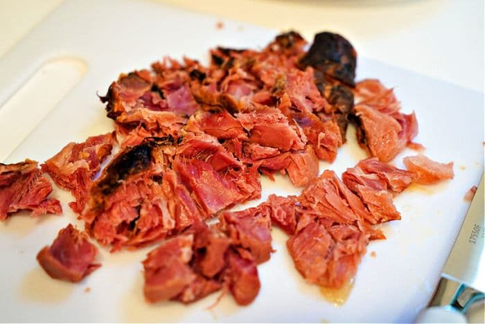 Chopped smoked ham hocks on a white cutting board, reminiscent of how to cook ham hocks in a slow cooker, ready for serving.