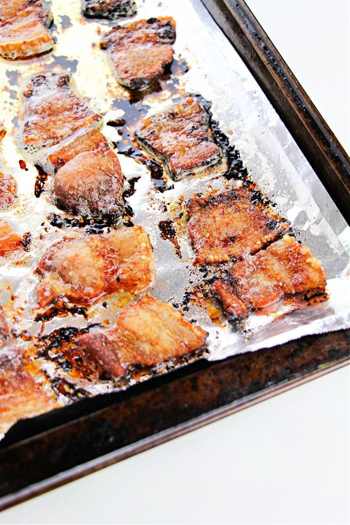 Crispy bacon pieces on a foil-lined baking sheet, some edges charred and glistening with grease—this is a solid example of how to cook pork belly in the oven for that irresistible crunch.
