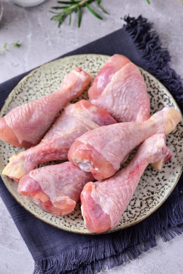 Raw chicken drumsticks on a speckled plate, ready to be seasoned after learning how to defrost chicken in the microwave, rest on a dark fabric napkin.