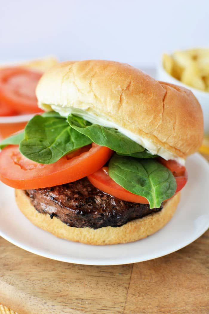 A hamburger with lettuce, tomato, and mayonnaise on a bun, served on a white plate—solid inspiration if you're learning how to grill frozen burgers to juicy perfection.