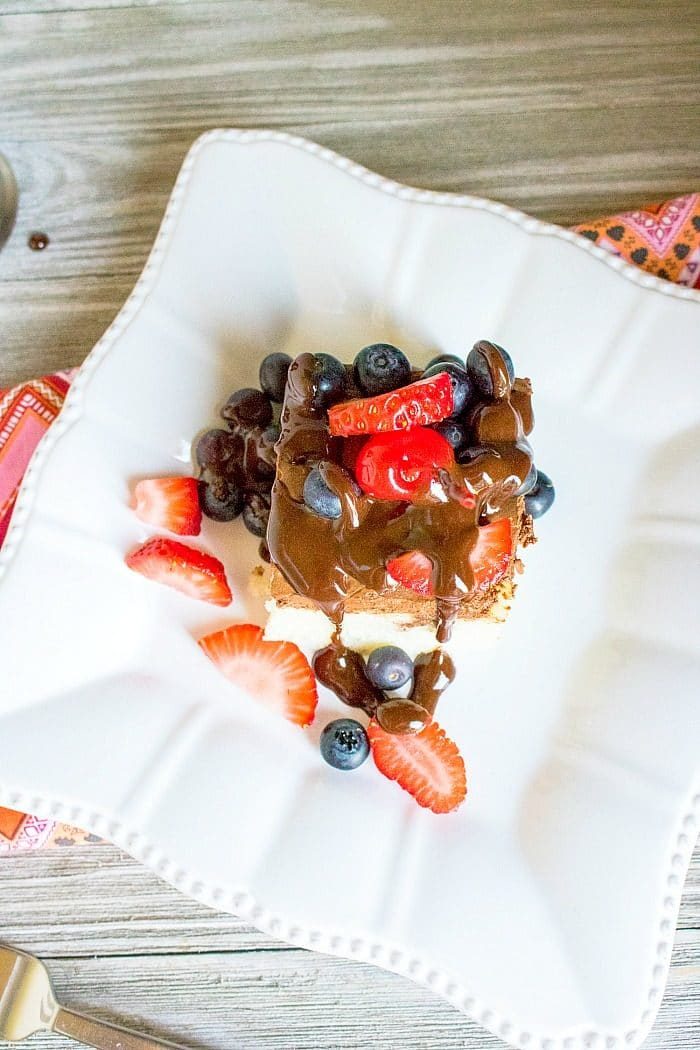 poke cake topped with chocolate sauce, strawberries, and blueberries on a white plate with a patterned napkin nearby, this delightful treat might inspire you to explore how to make a poke cake next time.