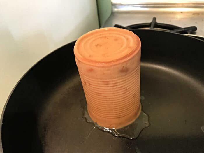 A can-shaped block of refried beans stands upright in a frying pan on the stove