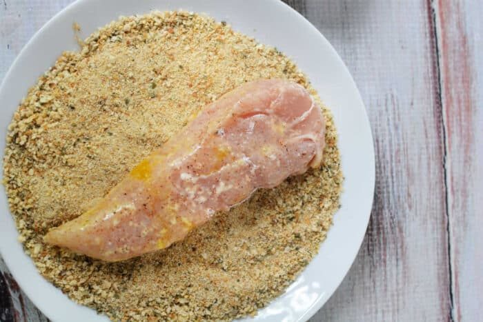 Learn how to make chicken tenders by breading raw chicken breast on a white plate, achieving that solid crispy texture.