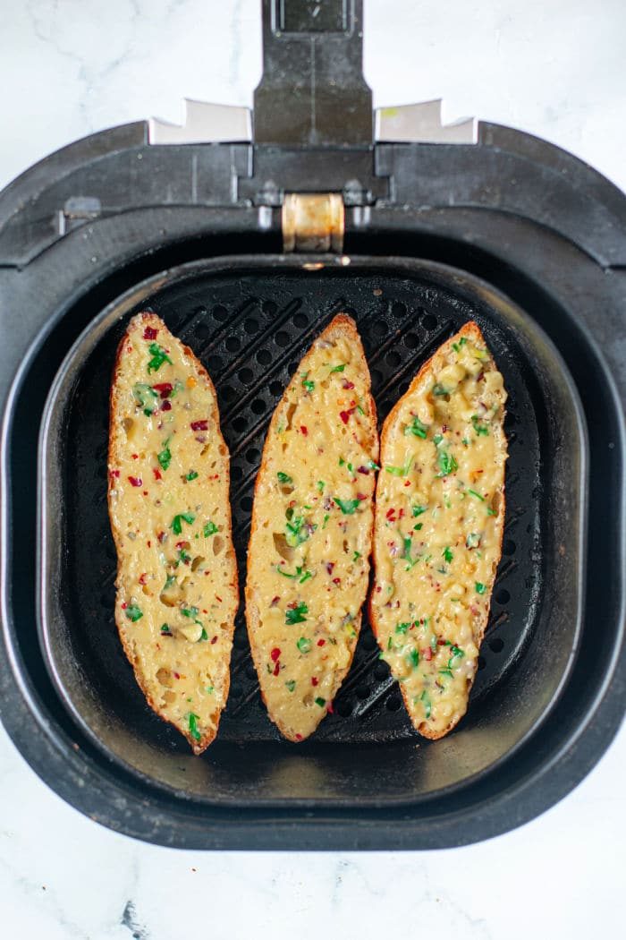 Three pieces garlic bread in an air fryer basket, garnished with herbs and spices, create a tempting aroma reminiscent of how to make garlic bread from scratch.