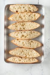 Sliced ciabatta bread with an airy texture on a metal baking sheet, solid for learning how to make garlic bread from scratch.