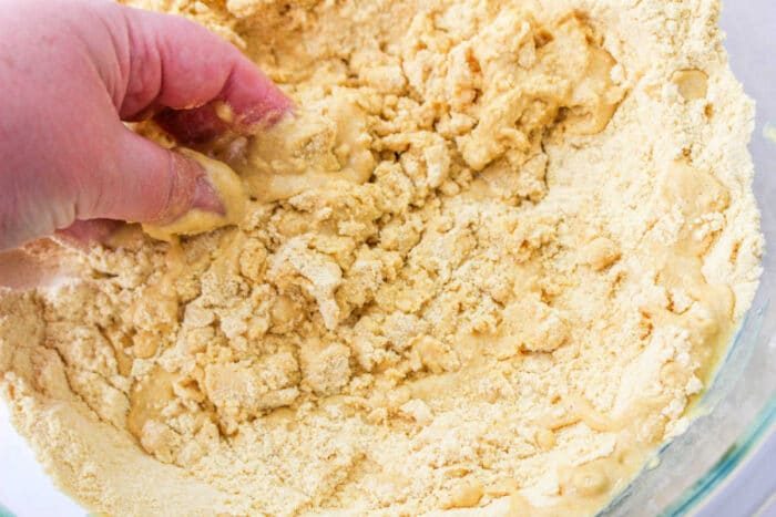 Hand mixing crumbly masa dough in a clear bowl, perfecting the art of how to make tamales masa.