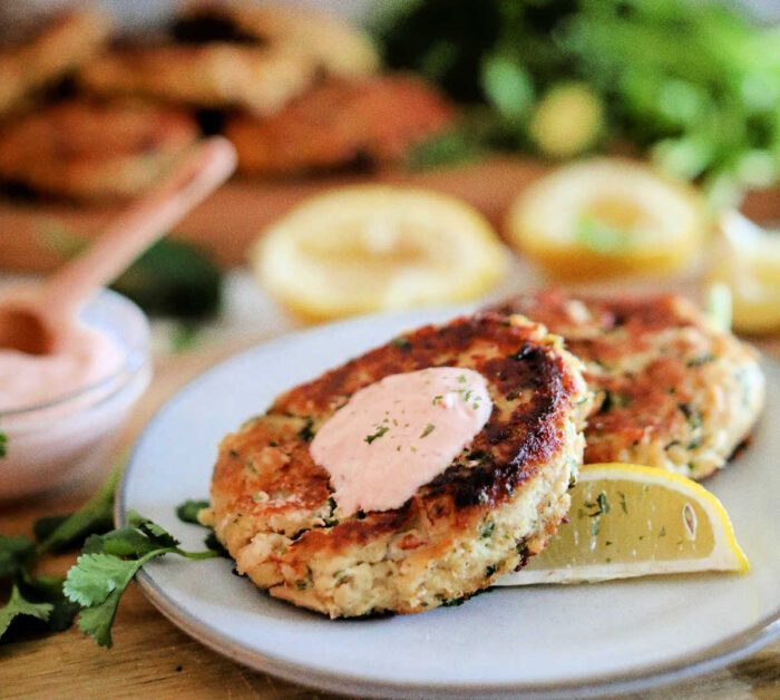 Two golden-brown patties with a dollop of sauce and a lemon wedge on a white plate, garnished with herbs—an appetizing presentation solid for anyone curious about how to make tuna patties.