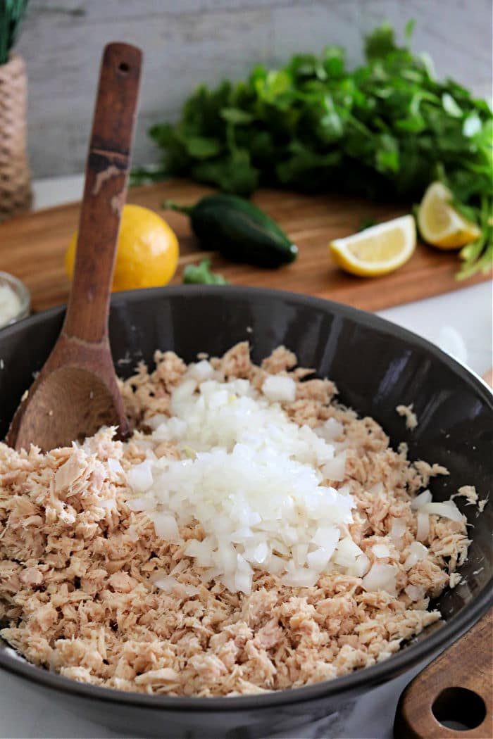 Chopped onions and shredded chicken in a bowl, with a wooden spoon; herbs and lemons in the background—like you'd gather your ingredients when learning how to make tuna patties, freshness is key for good results.