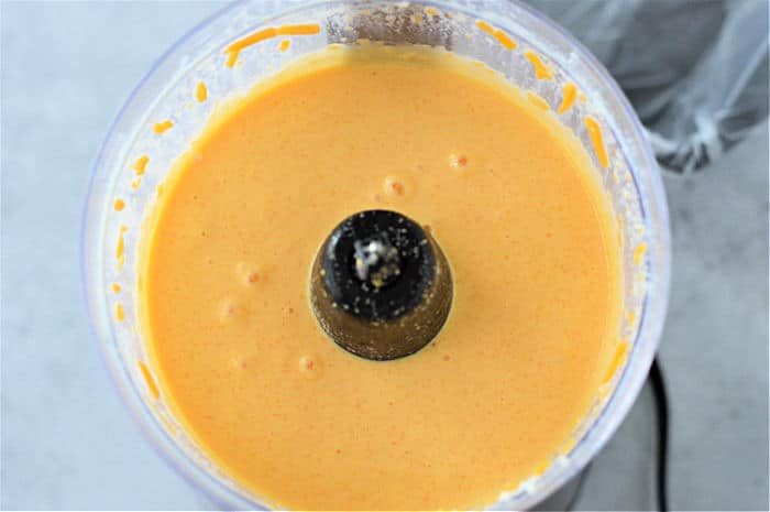 Blended cheese sauce mixture, reminiscent of a delectable Velveeta cheese sauce, swirled in a food processor bowl.