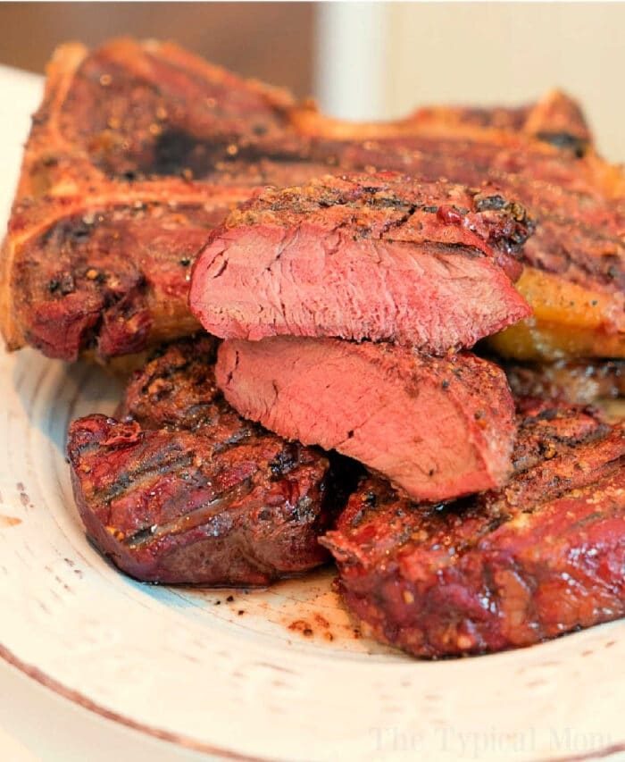 A plate featuring several slices of smoked steak at 250 degrees, showcasing a solid sear on the outside with a tender, pink interior. The seasoned steak is artfully arranged on a pristine white plate.