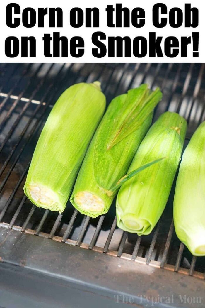 Three ears of corn in husks are placed on a smoker grill with text above that reads Corn on the Cob on the Smoker—showing how to smoke corn on the cob for good, smoky flavor!.