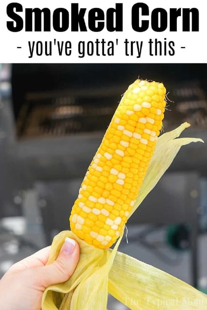 Hand holding a smoked ear of corn with text above that says, Smoked Corn - you've gotta try this. Discover how to smoke corn on the cob for a good twist.