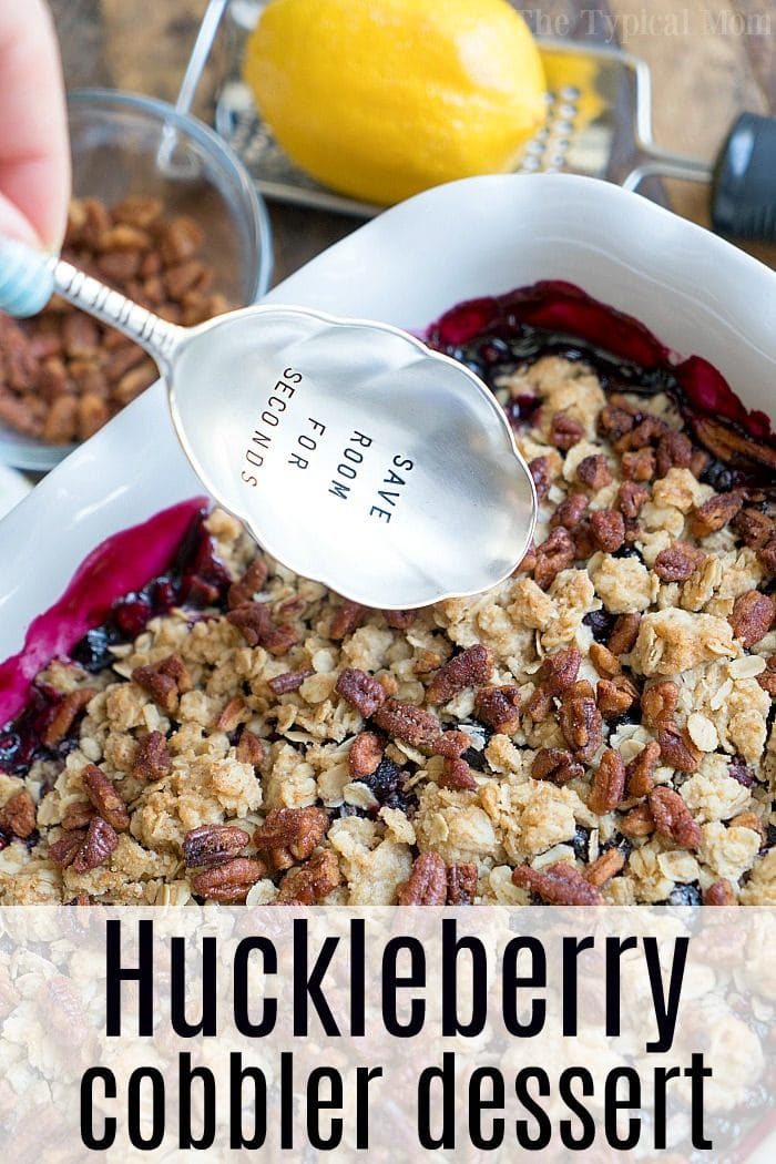 A spoon rests beside a generous serving of huckleberry cobbler in a white dish, with the words SAVE ROOM FOR SECONDS inviting you to enjoy every good bite.